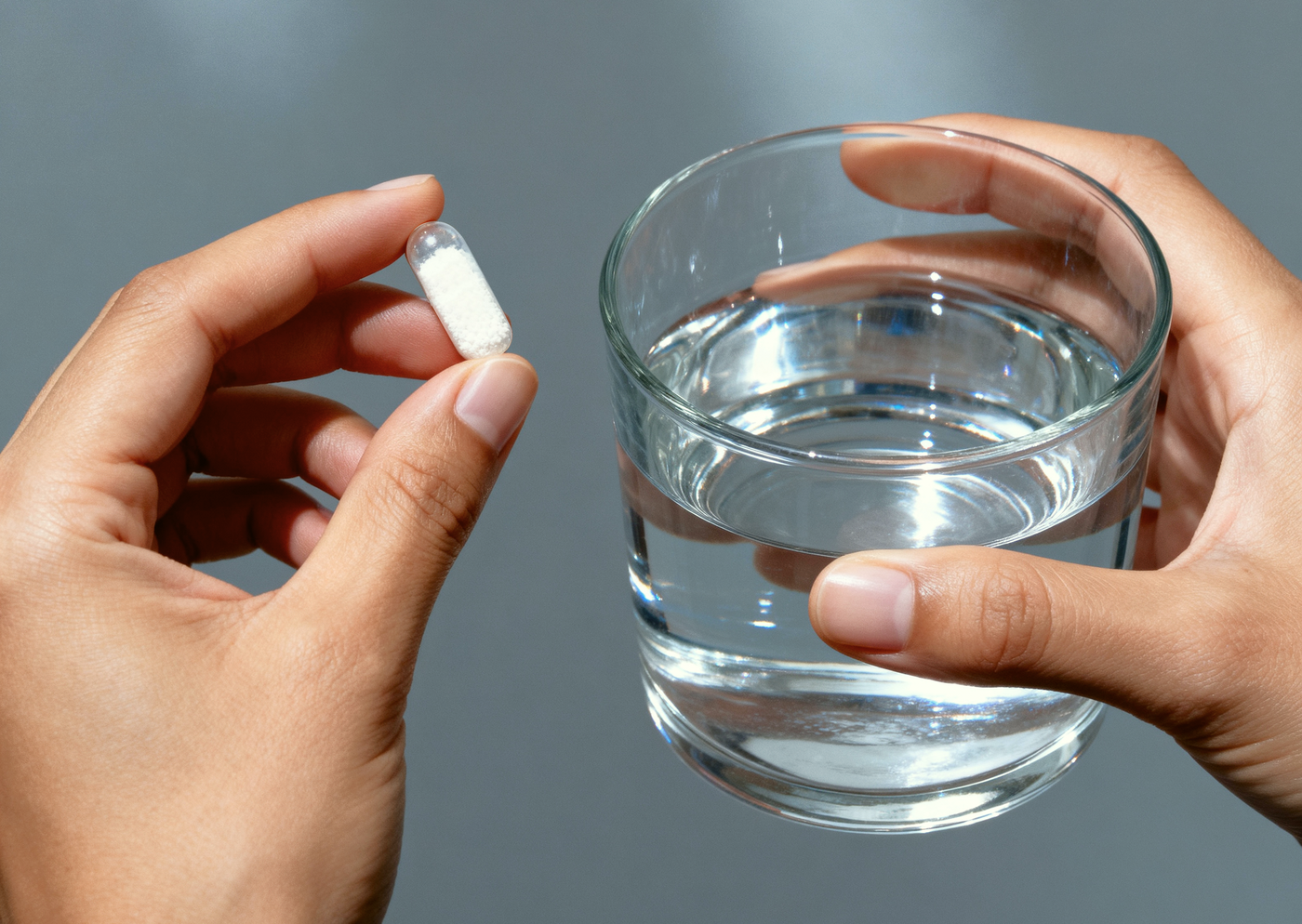 Hands holding a MadNutra RELAX capsule and a glass of water — the evening wind-down ritual